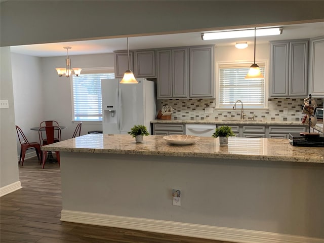 kitchen featuring decorative backsplash, light stone countertops, white fridge with ice dispenser, and decorative light fixtures