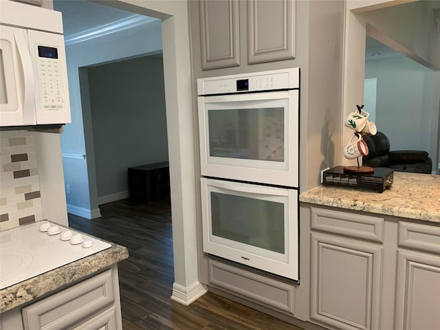 kitchen with white cabinetry, decorative backsplash, white appliances, dark wood-type flooring, and light stone counters