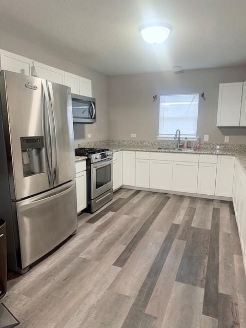 kitchen with sink, light stone counters, light hardwood / wood-style floors, white cabinets, and appliances with stainless steel finishes