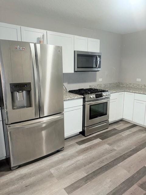 kitchen with light stone countertops, appliances with stainless steel finishes, light hardwood / wood-style flooring, and white cabinetry