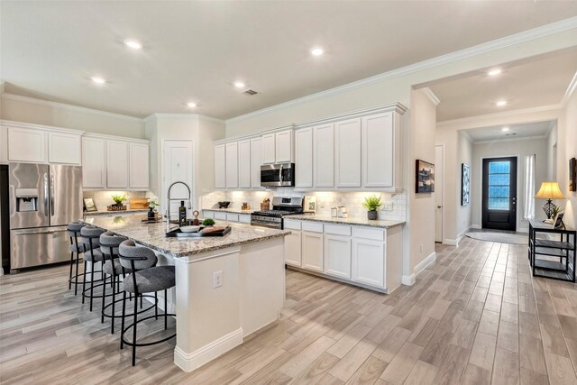 kitchen with light stone countertops, appliances with stainless steel finishes, white cabinets, and an island with sink