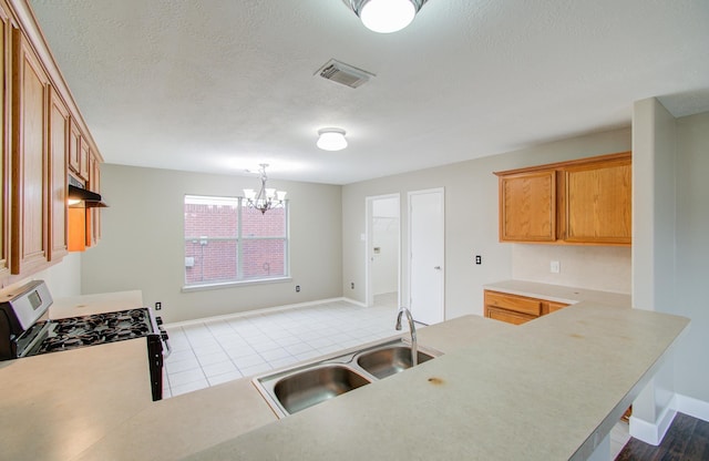 kitchen featuring an inviting chandelier, sink, light tile patterned floors, gas stove, and kitchen peninsula