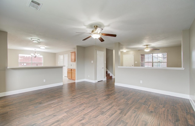 unfurnished living room featuring ceiling fan with notable chandelier and dark hardwood / wood-style floors