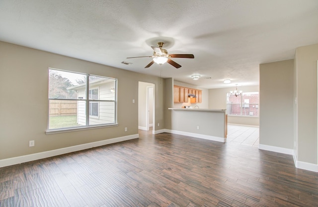 unfurnished living room featuring ceiling fan with notable chandelier and dark hardwood / wood-style flooring