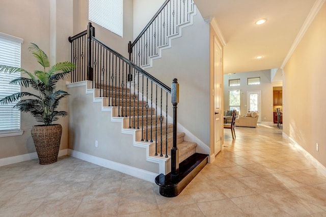 staircase with tile patterned floors, ornamental molding, and a high ceiling