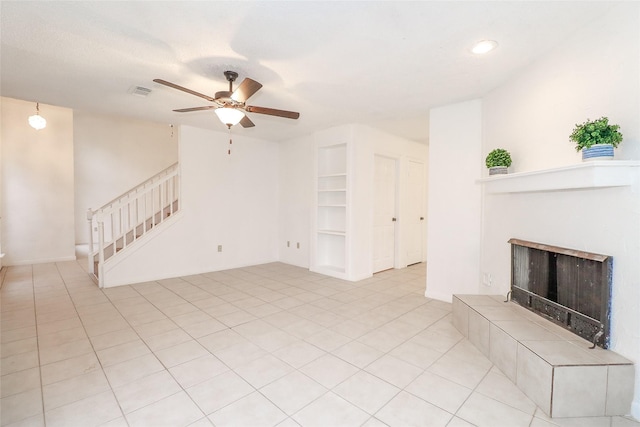 unfurnished living room with a tiled fireplace, ceiling fan, built in features, and light tile patterned floors