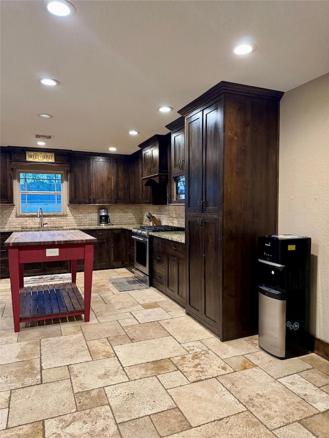 kitchen with dark brown cabinets, stainless steel range with gas stovetop, and tasteful backsplash