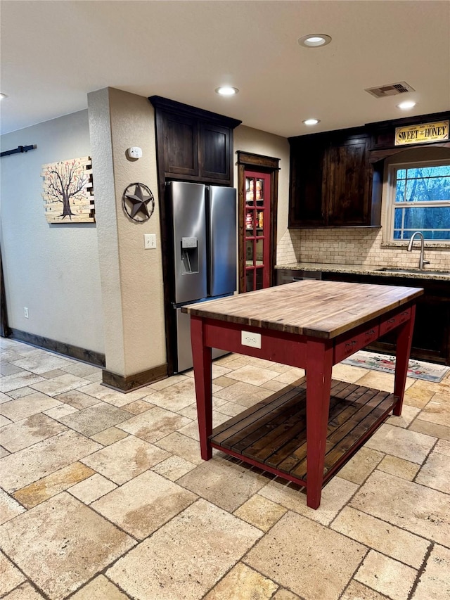 kitchen featuring stainless steel fridge, backsplash, dark brown cabinets, and sink