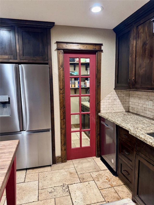 kitchen featuring light stone countertops, dark brown cabinetry, decorative backsplash, and stainless steel appliances