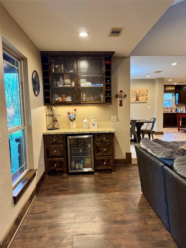 bar featuring dark hardwood / wood-style floors, light stone countertops, dark brown cabinetry, and beverage cooler