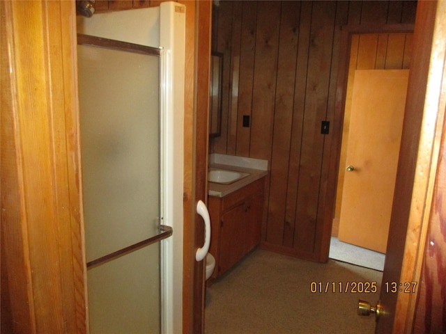 bathroom with vanity, a shower with door, and wood walls