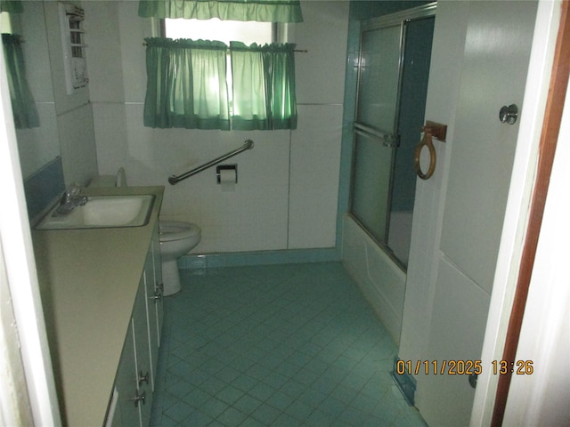 full bathroom with tile patterned floors, bath / shower combo with glass door, toilet, vanity, and tile walls