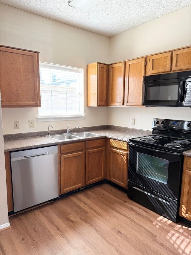 kitchen with sink, black appliances, a textured ceiling, and light hardwood / wood-style flooring