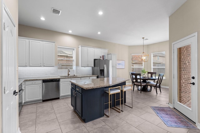 kitchen with sink, appliances with stainless steel finishes, tasteful backsplash, white cabinets, and a kitchen island