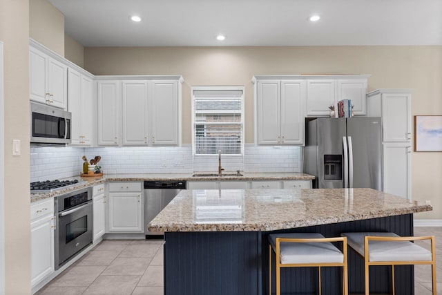 kitchen with appliances with stainless steel finishes, white cabinetry, sink, a center island, and light stone counters