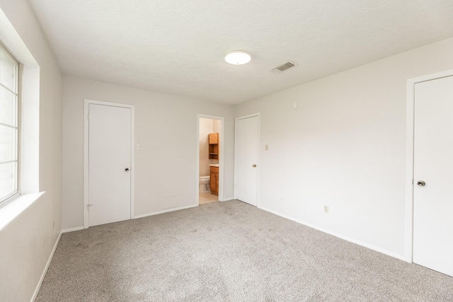 unfurnished bedroom featuring ensuite bath, carpet, and a textured ceiling