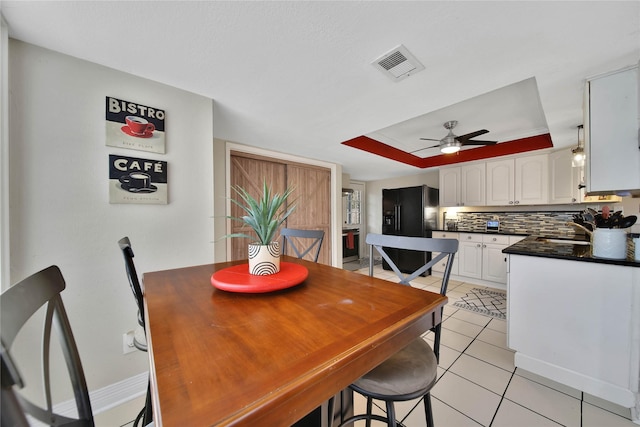 dining area featuring light tile patterned floors, ceiling fan, visible vents, baseboards, and a tray ceiling