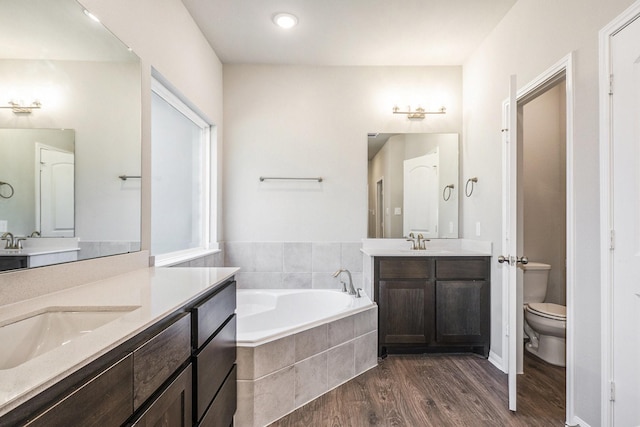 bathroom featuring tiled tub, hardwood / wood-style floors, vanity, and toilet