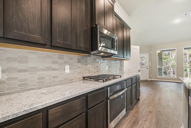 kitchen with tasteful backsplash, light stone counters, dark brown cabinetry, stainless steel appliances, and wood-type flooring