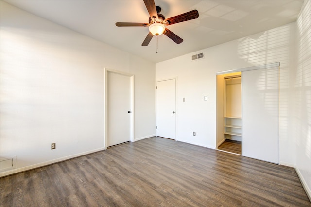 unfurnished bedroom with a walk in closet, ceiling fan, a closet, and dark hardwood / wood-style floors