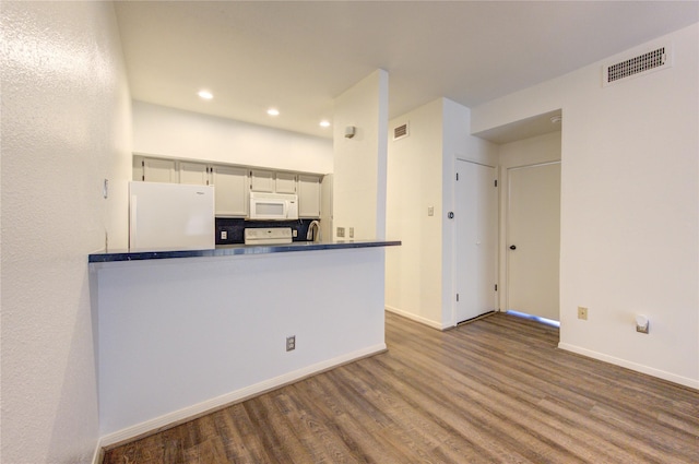 kitchen featuring white appliances, decorative backsplash, hardwood / wood-style flooring, and kitchen peninsula