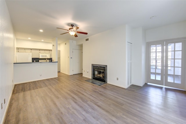 unfurnished living room featuring ceiling fan, light hardwood / wood-style flooring, french doors, and a tile fireplace