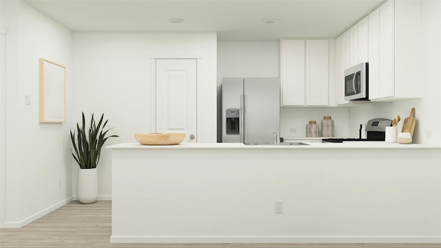 kitchen with kitchen peninsula, appliances with stainless steel finishes, sink, white cabinets, and light hardwood / wood-style floors