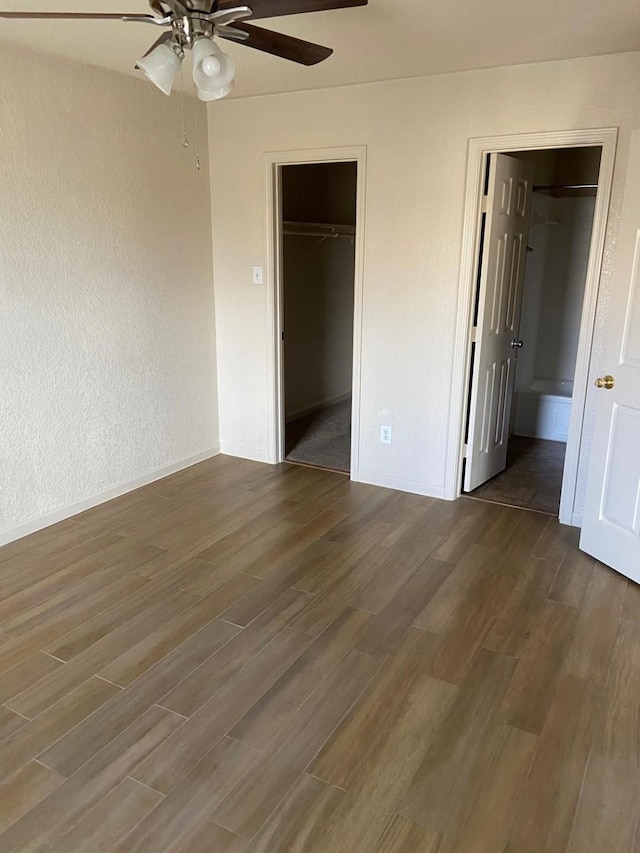 unfurnished bedroom with a spacious closet, a closet, ceiling fan, and dark hardwood / wood-style floors