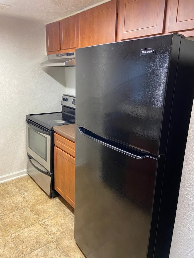 kitchen featuring stainless steel range with electric stovetop, black refrigerator, light tile patterned flooring, and a textured ceiling