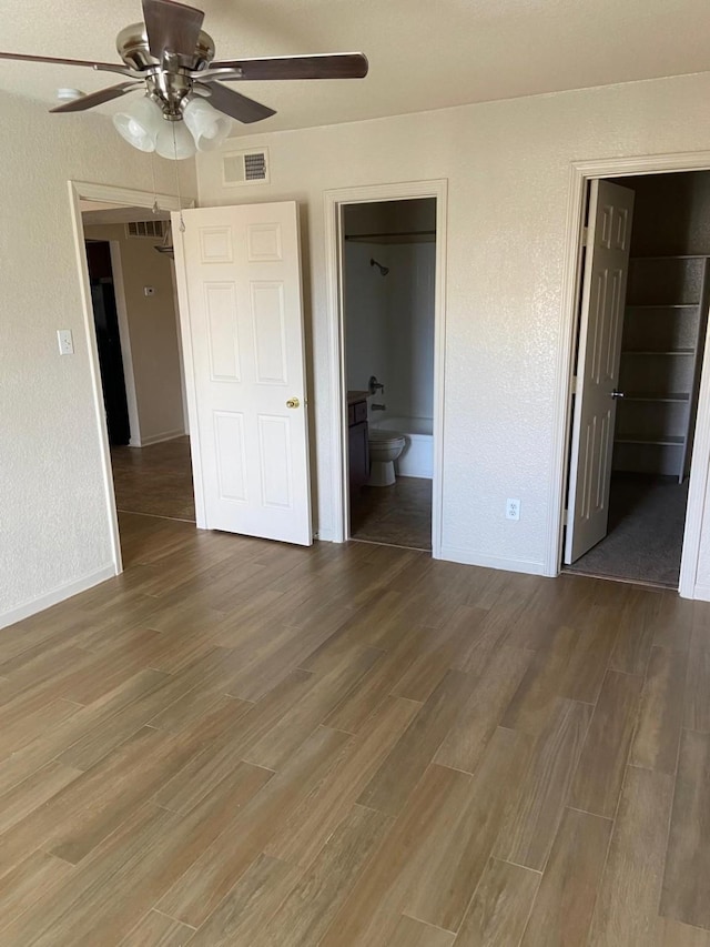 unfurnished bedroom featuring dark hardwood / wood-style flooring, ensuite bath, ceiling fan, a spacious closet, and a closet