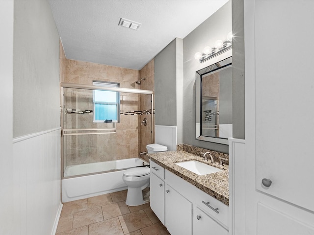 full bathroom featuring bath / shower combo with glass door, a textured ceiling, vanity, tile patterned flooring, and toilet