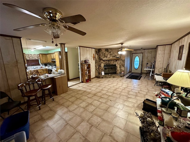 living room featuring wooden walls, a fireplace, ceiling fan, and a textured ceiling