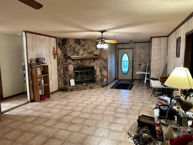 living room with wood walls, ceiling fan, ornamental molding, a textured ceiling, and a fireplace