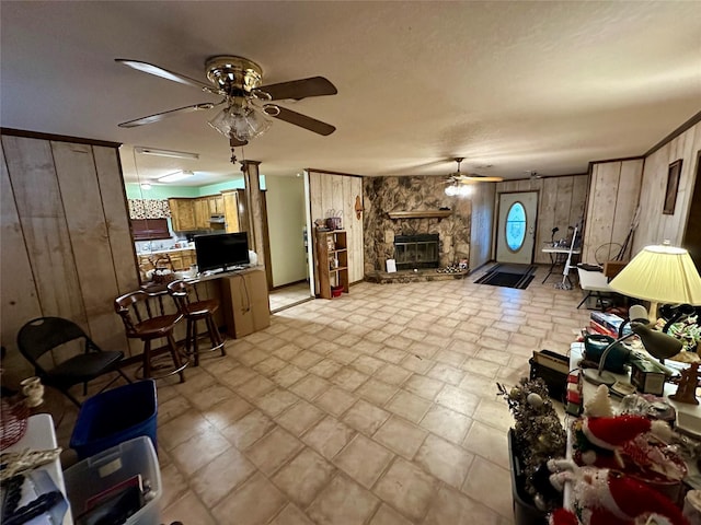 living room with ceiling fan, a stone fireplace, and wooden walls