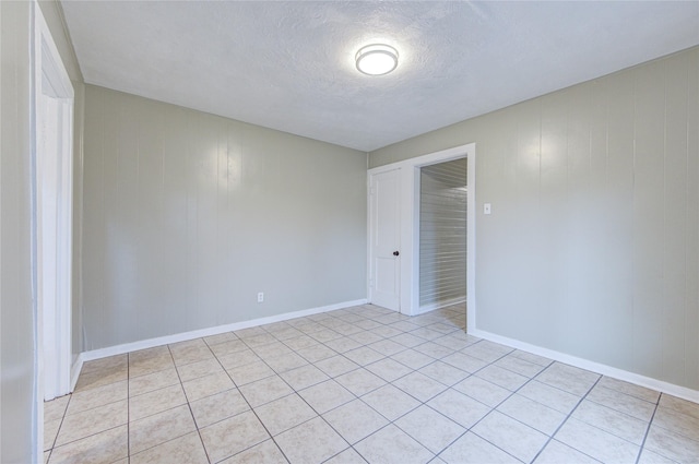 tiled empty room featuring wood walls and a textured ceiling