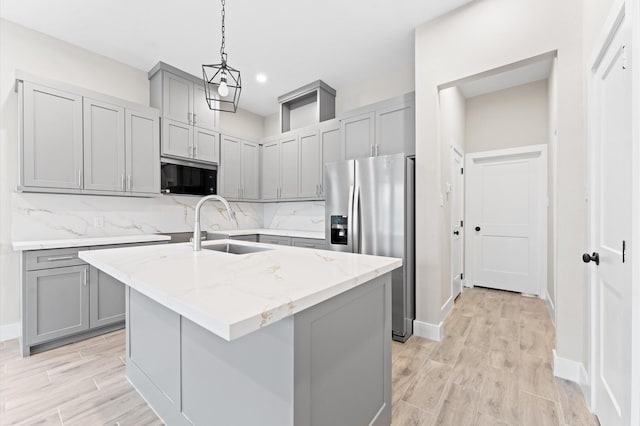 kitchen featuring a kitchen island with sink, sink, tasteful backsplash, light stone counters, and stainless steel fridge with ice dispenser