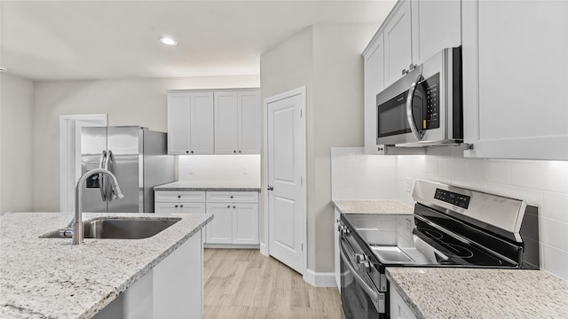 kitchen featuring backsplash, sink, appliances with stainless steel finishes, light hardwood / wood-style floors, and light stone counters