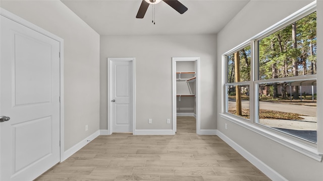 unfurnished bedroom with multiple windows, ceiling fan, light hardwood / wood-style flooring, and a walk in closet