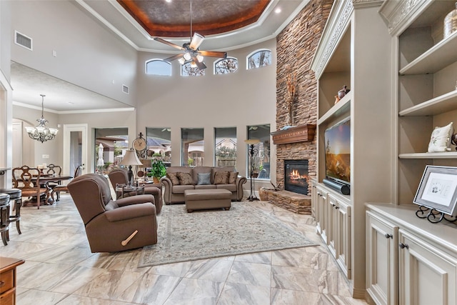 living room featuring a high ceiling, ceiling fan with notable chandelier, a stone fireplace, a raised ceiling, and built in shelves