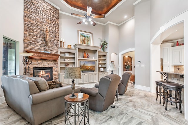 living room with a fireplace, a raised ceiling, ceiling fan, and crown molding