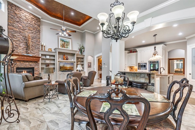 dining area with a high ceiling, ceiling fan with notable chandelier, sink, ornamental molding, and a fireplace