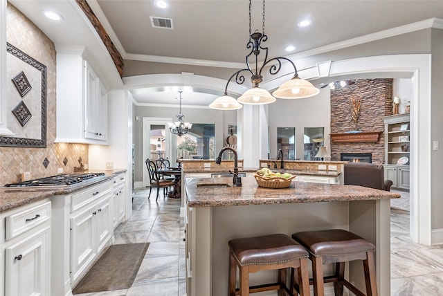 kitchen featuring stainless steel gas stovetop, a breakfast bar, a center island with sink, a fireplace, and decorative light fixtures