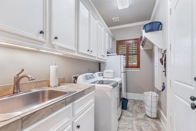 laundry room featuring washing machine and clothes dryer, sink, cabinets, a textured ceiling, and ornamental molding