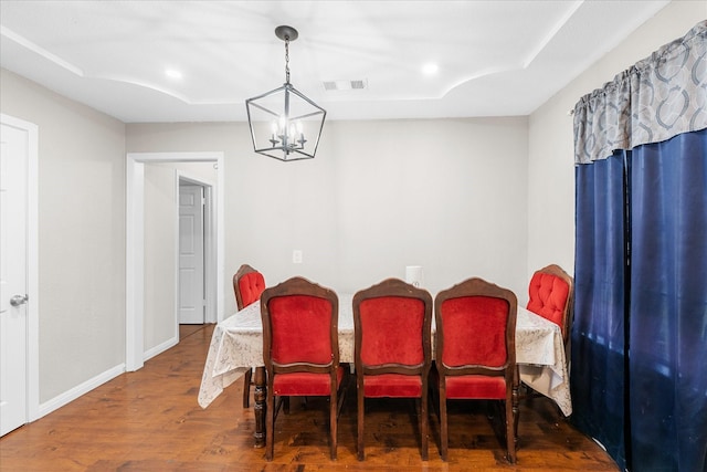 dining area featuring hardwood / wood-style floors, a notable chandelier, and a raised ceiling