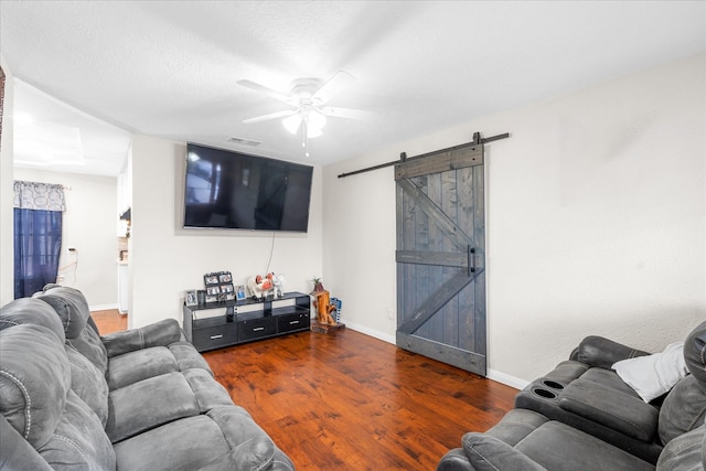 living room featuring a barn door, ceiling fan, dark wood-type flooring, and a textured ceiling