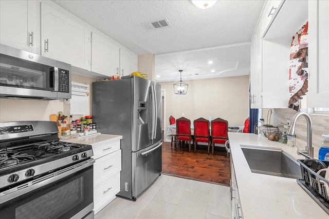 kitchen featuring white cabinetry, sink, stainless steel appliances, a textured ceiling, and decorative light fixtures