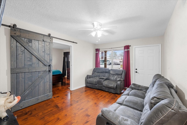 living room featuring a barn door, ceiling fan, dark wood-type flooring, and a textured ceiling