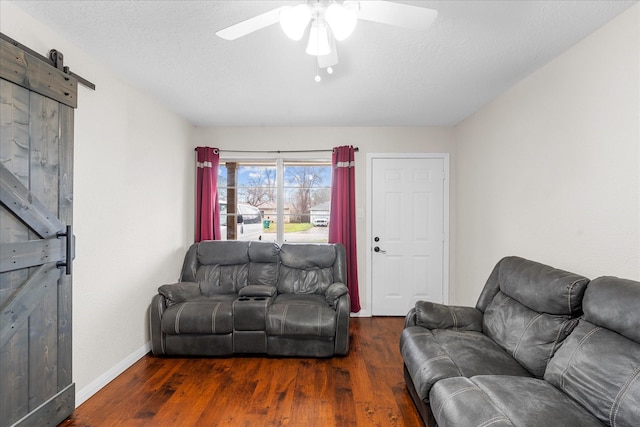 living room featuring a barn door, ceiling fan, dark hardwood / wood-style flooring, and a textured ceiling