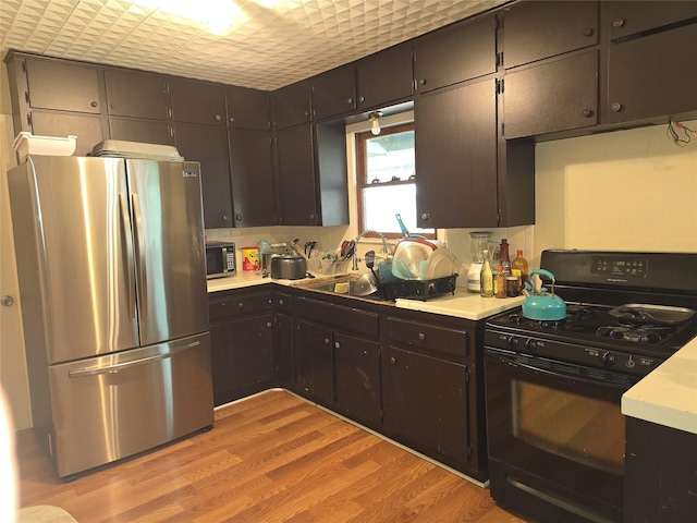 kitchen featuring sink, stainless steel fridge, light hardwood / wood-style floors, dark brown cabinetry, and gas stove