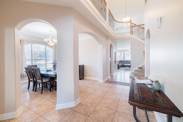 tiled entryway featuring ornamental molding, a high ceiling, and a notable chandelier